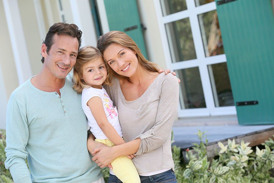 Personal Insurance - Smiling Young Family With Daughter Standing Outside Their Home